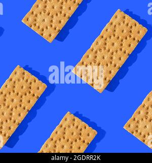 Foto in Form eines nahtlosen Musters. Orangefarbene Chips für gesunde Lebensmittel mit Schatten auf blauem Hintergrund. Stockfoto