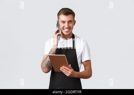 Einzelhandelsgeschäfte, kleine Unternehmen, Cafés und Restaurants Takeaway Konzept. Gut aussehender lächelnder Verkäufer, Barista, der telefoniert, glücklich lacht, nimmt Stockfoto