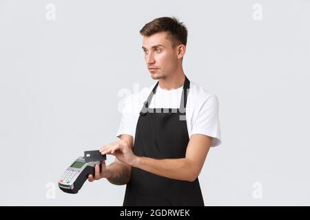 Einzelhandel, Café und Restaurant, Mitarbeiter Konzept. Schöner Barista in schwarzer Schürze, Kellner übergab POS-Terminal für Zahlung und Kreditkarte Stockfoto