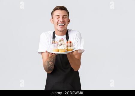 Kleineinzelhandel, Cafés und Bäckereikonzept. Gut aussehender Barista, Arbeiter im Laden oder Kellner, der köstliche Desserts zeigt und schmackhaft verkauft Stockfoto