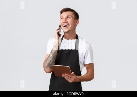 Einzelhandelsgeschäfte, kleine Unternehmen, Cafés und Restaurants Takeaway Konzept. Gut aussehender lächelnder Verkäufer, Barista, der telefoniert, glücklich lacht, nimmt Stockfoto