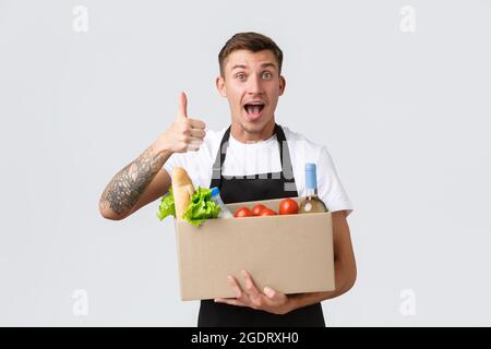 Einzelhandel, Lebensmitteleinkauf und Lieferkonzept. Schöner Kurier in schwarzer Schürze überreicht Box mit Lebensmitteln, Verkäufer vorbereitet Paket für Stockfoto