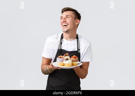 Kleineinzelhandel, Cafés und Bäckereikonzept. Leidenschaftlicher, gutaussehender Barista, Verkäufer im Konditorladen, enge Augen und lächelnd Stockfoto