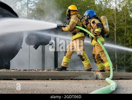 Feuerwehrleute der lettischen Bundeswehr und der estnischen Streitkräfte verwenden einen Löschschlauch, um ein simuliertes Flugzeugfeuer im Alpena Combat Readiness Training Center, Michigan, am 12. August 2021, zu sprühen. Die Simulation war Teil der Übung Northern Strike 21-2, einer der größten Übungen des Verteidigungsministeriums zur Bereitschaft von Reservekomponenten, die zwei Wochen lang im National All-Domain Warfighting Center im Norden von Michigan durchgeführt wird. (USA Foto der Air National Guard von Staff Sgt. Valentina Viglianco) Stockfoto
