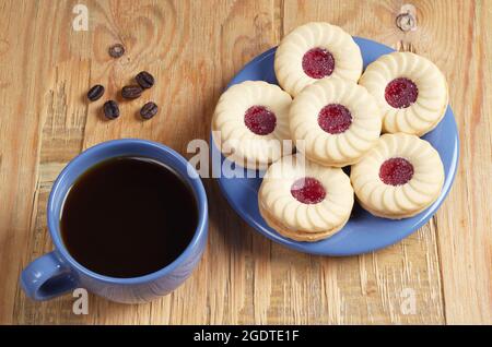 Tasse Kaffee und Kekse mit Marmelade in blauem Geschirr auf rustikalem Holztisch Stockfoto