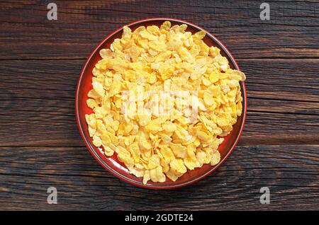 Maisflocken in roter Platte auf dunklem Holzhintergrund, Draufsicht Stockfoto