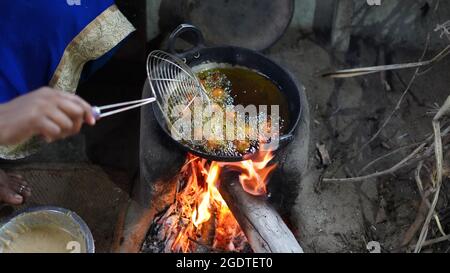 Frau braten Lebensmittel mit Senföl auf dem Ofen. Typischer Holzofen oder Chulha, der im ländlichen indien zum Kochen verwendet wird. Stockfoto