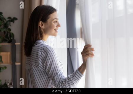 Lächelnde Frau schaut im Fenster und denkt träumend Stockfoto