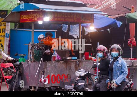 Zwei kambodschanische Frauen, die Schutzmasken / Abdeckungen tragen, warten während der Coronavirus-Pandemie auf ihr gebratenes Schweinefleisch. Kandal Market, Phnom Penh, Kambodscha. August 2021. © Kraig Lieb Stockfoto