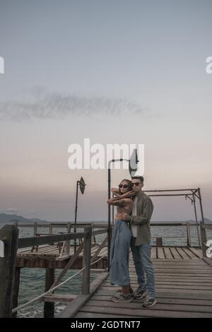 Ein verliebtes Paar, das auf einem alten hölzernen Pier steht und kuschelt. Tragen von Sonnenbrillen und legerer Kleidung. Meerblick. Hochwertige Fotos. Stockfoto