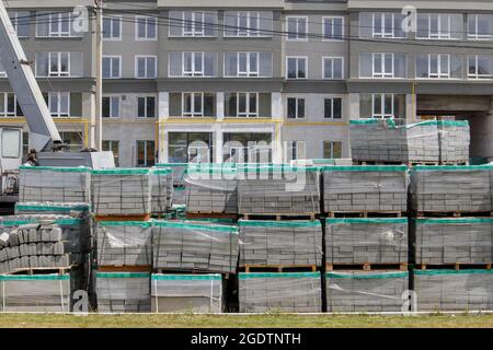 Auf der Baustelle befinden sich viele neue graue Pflasterplatten auf kunststoffgedeckten Paletten. Pflaster von Fußgängerwegen auf einer Stadtstraße. Vordergrund. Rep Stockfoto