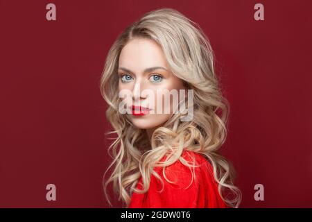 Blonde lockige lange Haare Frau mit Schönheit Make-up auf rotem Hintergrund Stockfoto