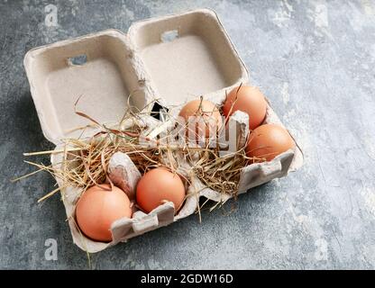 Eier auf Heu im Papierbehälter. Grauer Stein, rauer Hintergrund. Stockfoto