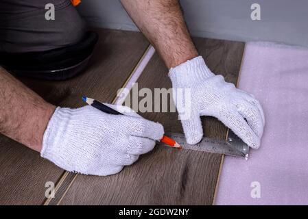 Konzept der Heimwerkerverbesserung. Handwerker mißt und markiert die neue Laminatplatte für den Schnitt. Stockfoto