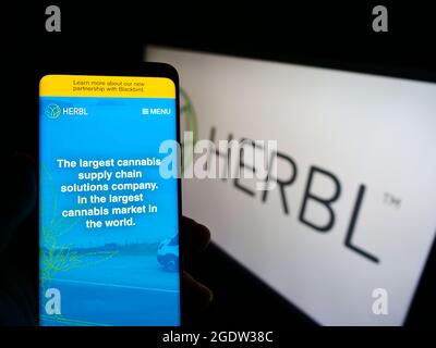 Person mit Smartphone und Website des amerikanischen Cannabis-Lieferkettenunternehmens HERBL auf dem Bildschirm vor dem Logo. Konzentrieren Sie sich auf die Mitte des Telefondisplays. Stockfoto