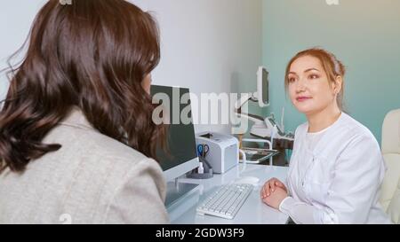 Junge Frau spricht mit einem glücklichen Arzt, der am Tisch im Büro sitzt Stockfoto