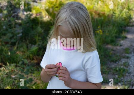 Blonde Kleinkind Mädchen erkunden Wildblumen an den sonnigen Sommertag. Pflanzen in den Händen Stockfoto