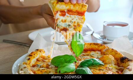 Die Hände einer jungen Frau nehmen Pizzastücke und legen sie im Café auf den Teller Stockfoto