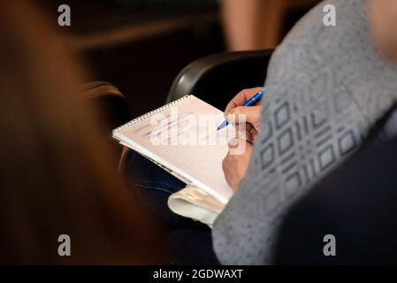 Der Mann macht sich Notizen in einem Notizbuch, während er auf einer Pressekonferenz sitzt Stockfoto