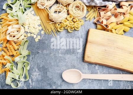 Holzschneidebrett und gemischte Arten und Formen von italienischen Pasta auf grauem Stein Hintergrund. Speicherplatz kopieren. Stockfoto