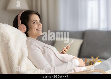 Lächelnde Schwangerin in kabellosen Kopfhörern, die Musik hören Stockfoto