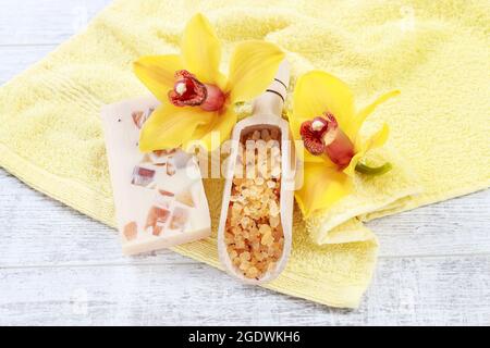 Kugel Meersalz, ein Stück handgemachte Seife und zwei gelbe Orchideenblumen. Spa-Set auf weißem Holztisch. Stockfoto