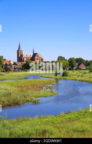 Blick über grünes Feuchtwasser auf das Stadtbild der Stadt durch mit Turm einer mittelalterlichen Kirche gegen blauen Sommerhimmel - Neer (Limburg), Niederlande Stockfoto