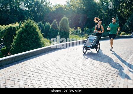 Familie mit Kind läuft mit einem Jogging-Kinderwagen durch einen Stadtpark Stockfoto