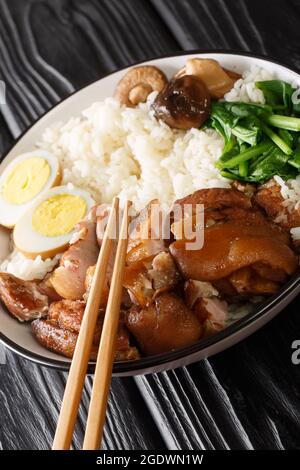 Geschmortes Schweinekeul mit Reis, Eiern und Kräutern Thai Khao Kha Moo in der Schüssel auf dem Tisch. Vertikal Stockfoto