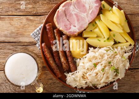 Deutscher Kassler-Schweinehals mit Sauerkraut-Kartoffeln und leichtem Bier auf Holztisch aus der Nähe. Horizontale Draufsicht von oben Stockfoto