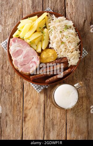 Geräucherter Kassler-Schweinehals und gebratene Würste mit Sauerkraut-Kartoffelpüree und Senf sowie leichter Bieraufnahme auf Holzhintergrund. Vertikal oben Vie Stockfoto