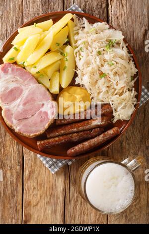 Kassler und Würstchen mit Sauerkraut, gekochten Kartoffeln und leichtem Bier aus nächster Nähe auf Holzhintergrund. Vertikale Draufsicht von oben Stockfoto