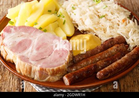 Deutscher Kassler Schweinehals mit Sauerkraut-Kartoffeln und Senf auf Holztisch Nahaufnahme in den Teller auf dem Tisch. Horizontal Stockfoto