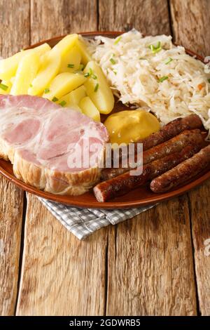 Geräucherter Kassler-Schweinehals und gebratene Würstchen mit Sauerkraut-Kartoffelpüree und Senf auf Holztisch in der Nähe des Tellers auf dem Tisch. Vertikal Stockfoto