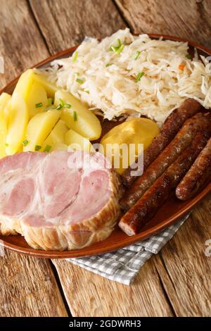 Kassler und Würstchen mit Sauerkraut und gekochten Kartoffeln in der Nähe auf dem Teller auf dem Tisch serviert. Vertikal Stockfoto