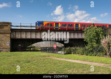 Ein Pendlerzug der South Western Railway, der über den Fluss Wandle, einem Nebenfluss der Themse, in Wandsworth, London, England, Großbritannien, fährt Stockfoto