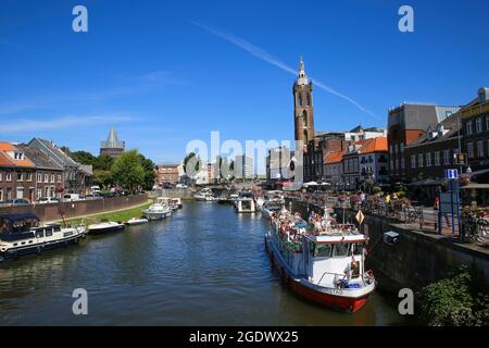 Roermond, Niederlande - Juli 9. 2021: Blick auf den geschäftigen holländischen Wasserkanal mit Stadtbild und altem Kirchturm vor blauem Sommerhimmel Stockfoto