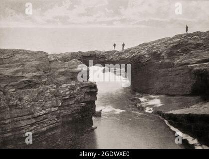 Eine Ansicht von Touristen aus dem späten 19. Jahrhundert auf einer natürlichen Felsbrücke an den Küstenklippen in der Nähe von Kilkee, einem Küstenort in der Grafschaft Clare, Irland. Stockfoto