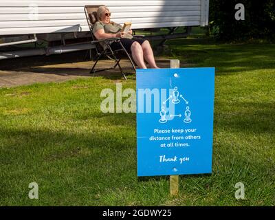 Eine Frau saß in der Sonne im Weymouth Bay Haven Holiday Park und las ein Buch. Stockfoto