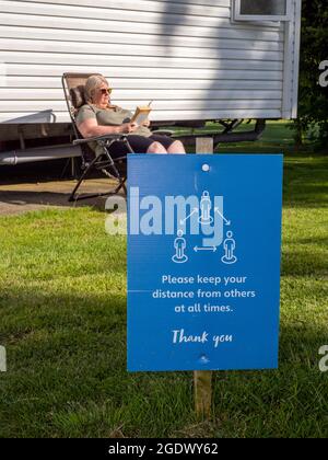 Eine Frau saß in der Sonne im Weymouth Bay Haven Holiday Park und las ein Buch. Stockfoto