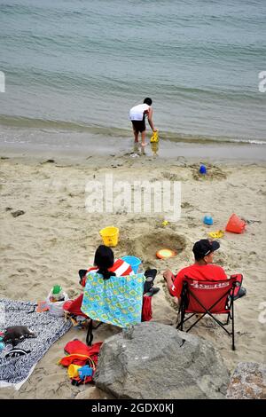 Junge Eltern beobachten ihren Sohn im Ozean von Moro Bay, während er im sehr kalten Pazifischen Ozean spielt Stockfoto