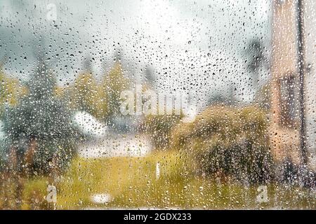 Herbstansicht aus dem Fenster, Regentropfen auf Glas, verschwommener Wolkenhimmel-Hintergrund. Stockfoto