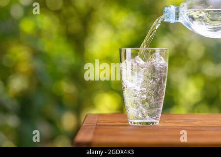 Wasser aus der Plastikflasche, das mit Eiswürfeln in das Glas gegossen wird Stockfoto