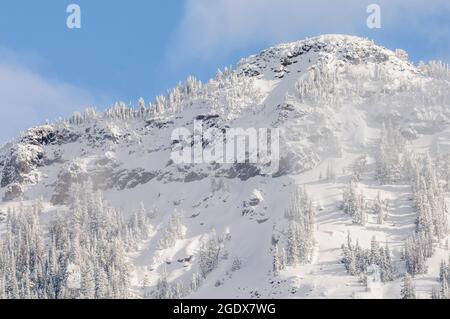 Schneebedeckter Berggipfel mit Nebel und Frost auf den Bäumen unter blauem Himmel Stockfoto