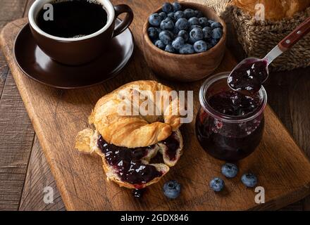 Croissant mit Heidelbeermarmelade und frischen Heidelbeeren auf einem rustikalen Holztisch Stockfoto