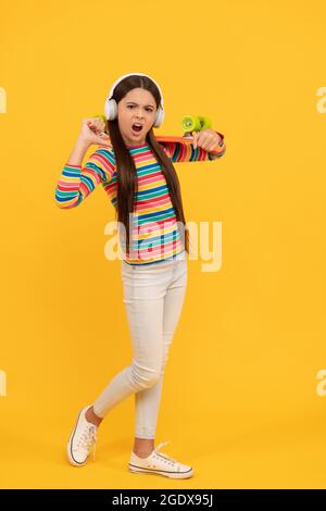 Unglücklicher Kinder-Skateboarder hört Musik in Kopfhörern mit Penny Board Skateboard, Hipster Stockfoto
