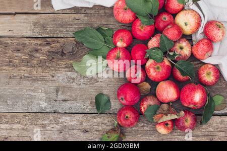 Rote Äpfel sind auf einem hellen Tuch auf einem Holztisch verstreut. Herbststimmung, Herbstschwingungen und -Farben, Mode und Stil des Herbstes Stockfoto