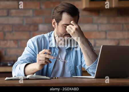 Müder Mann, der am Laptop arbeitet, leidet unter verschwommener Sicht Stockfoto