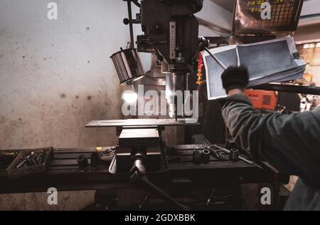 Fräsmaschine, die mit Handschuhen in der Nähe des Arbeiters arbeitet. Werkzeug zum Schneiden von Metallwerkstücken. Vertikale Fräsmaschine mit Wolfram Hartmetall-Fräser. Stahl Stockfoto