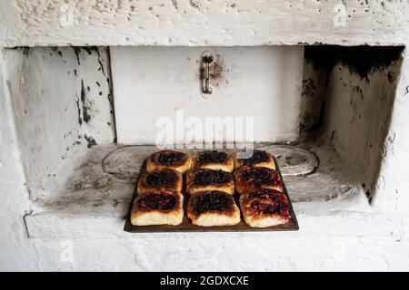 Köstliche Pasteten mit Beerenfüllung liegen auf einem Holzschneidebrett, auf einem russischen Ofen. Traditionelle Küche. Stockfoto